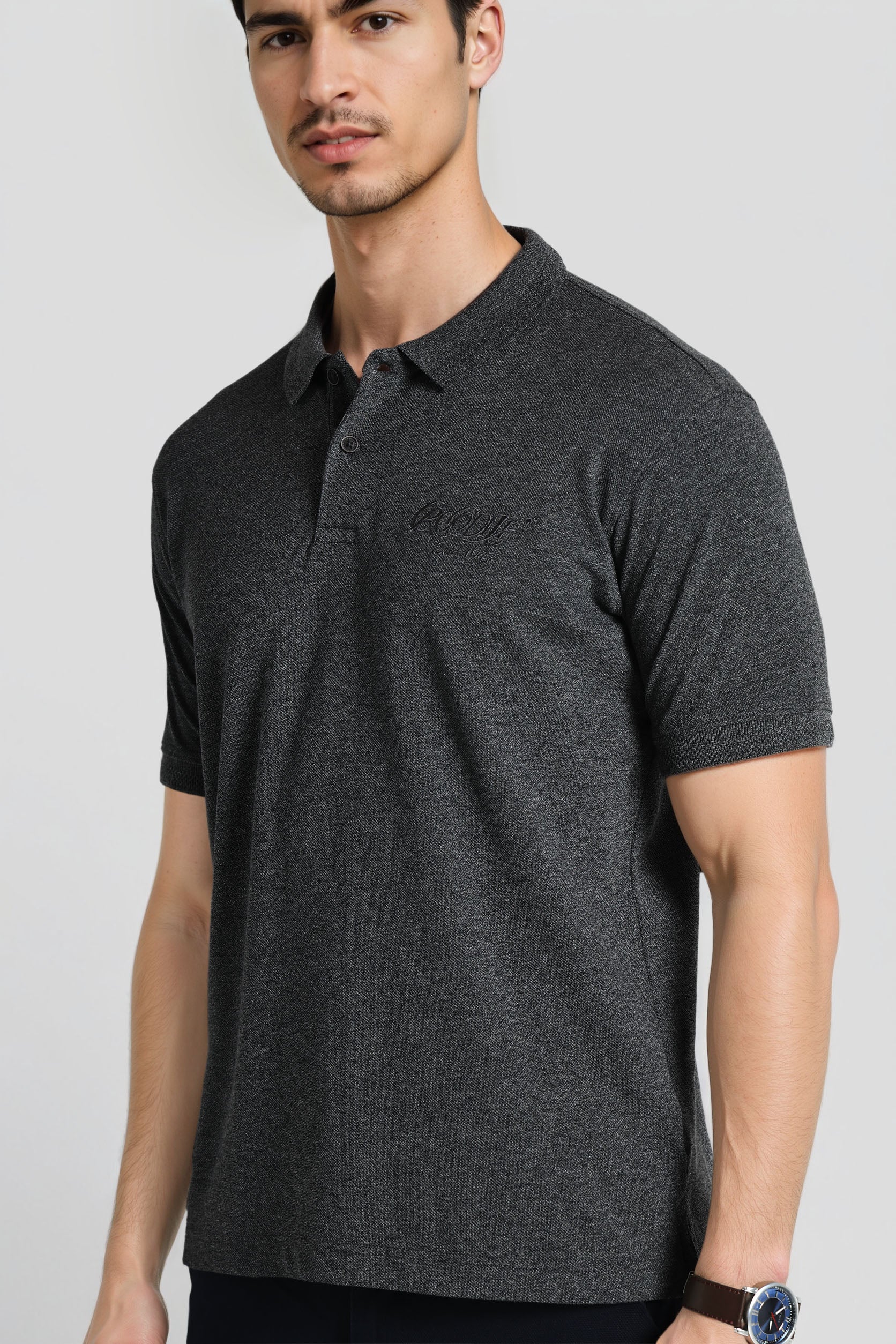Man wearing a dark gray polo shirt with a brand logo on a light gray background