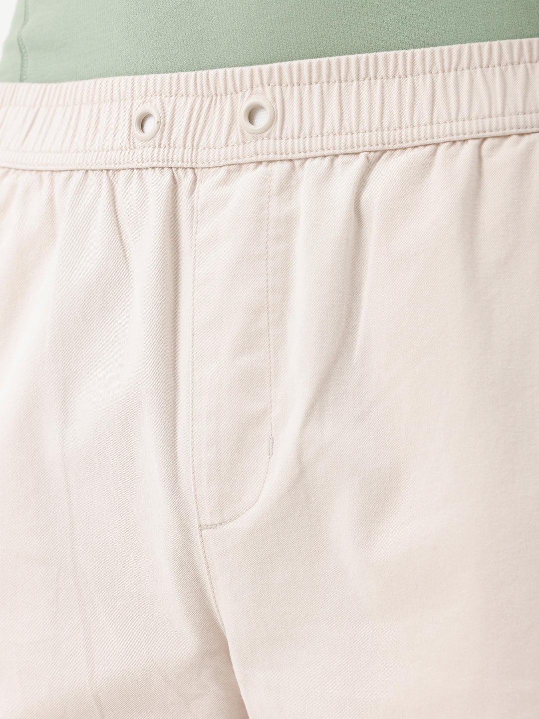 A man wearing light beige chino shorts, a sage green t-shirt, and brown suede loafers, shown from the waist down against a white studio background.