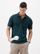 A man wearing a dark teal short-sleeve polo shirt with a chest pocket, paired with beige cargo pants, standing against a plain white studio background.