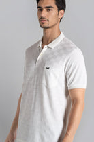 Man wearing a white polo shirt with a small logo on a gray background