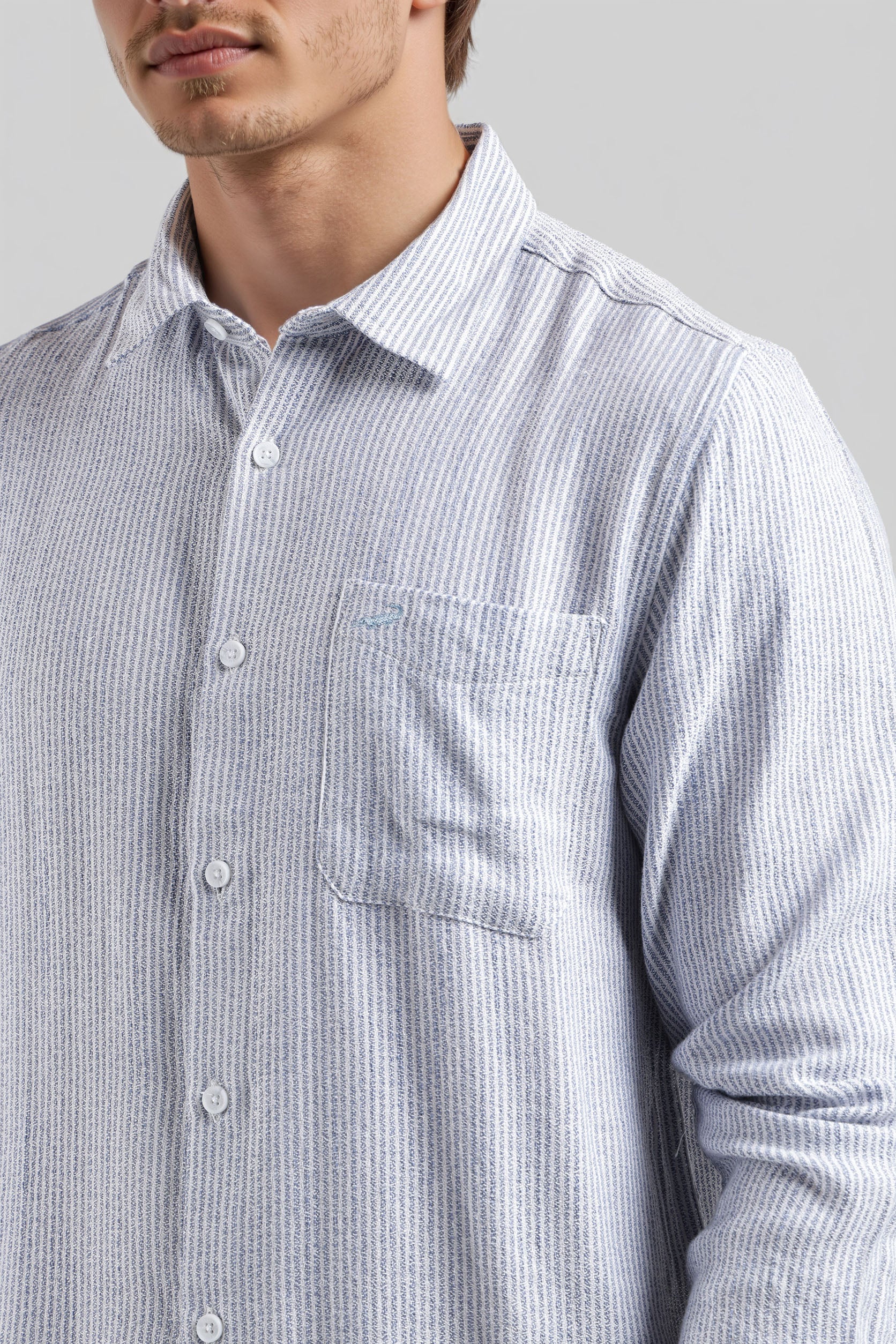 Close-up of a person wearing a light blue and white striped shirt with a pocket on a gray background