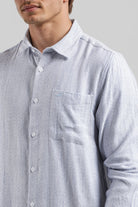 Close-up of a person wearing a light blue and white striped shirt with a pocket on a gray background
