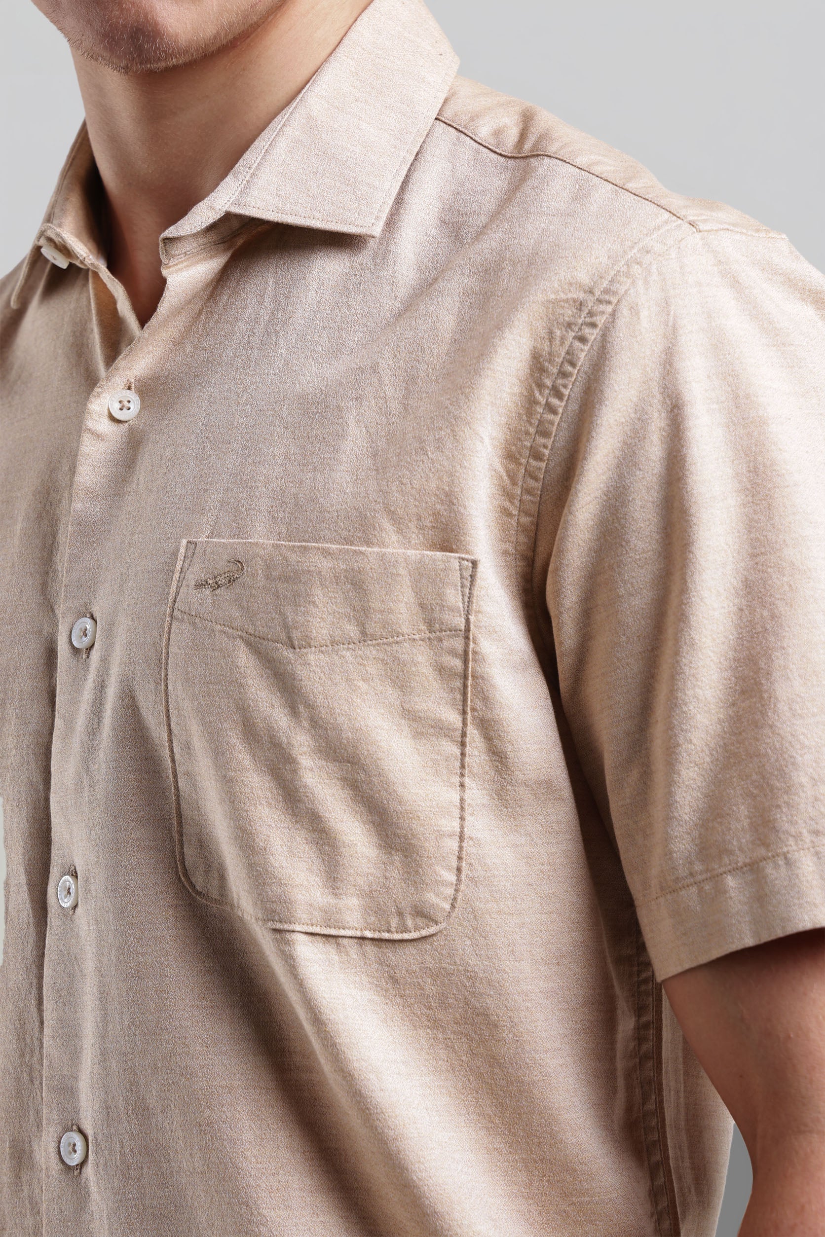 Close-up of a beige short-sleeve shirt with a pocket on a neutral background