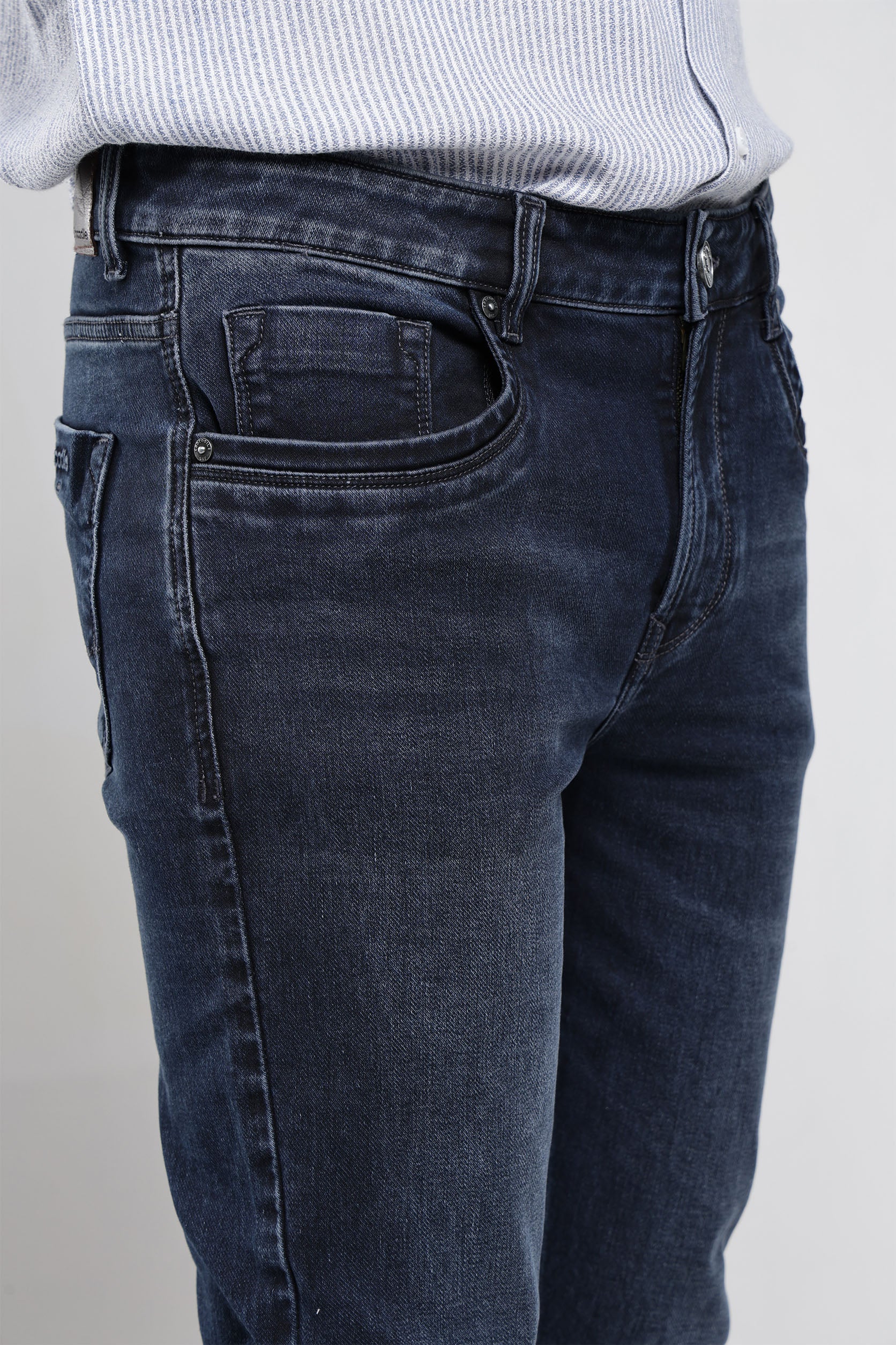 Dark blue jeans worn by a person on a plain background