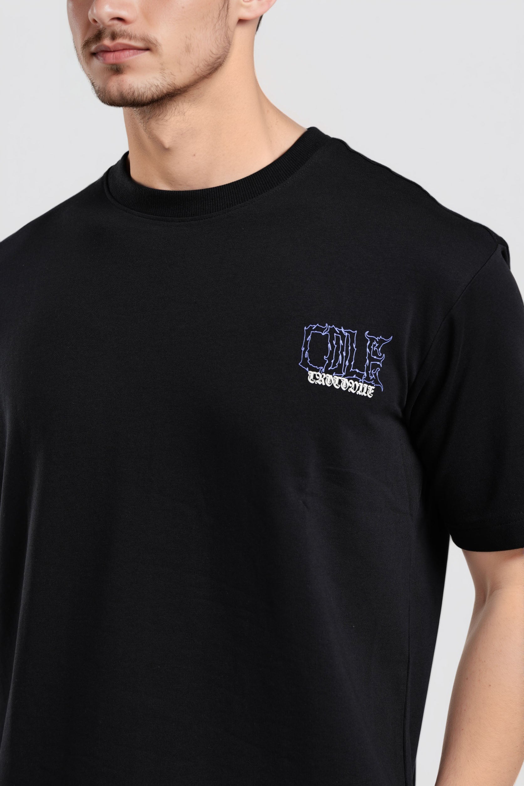 Black t-shirt with a small logo on the chest worn by a person against a plain background