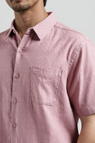Close-up of a person wearing a pink short-sleeve shirt with a pocket on a light gray background