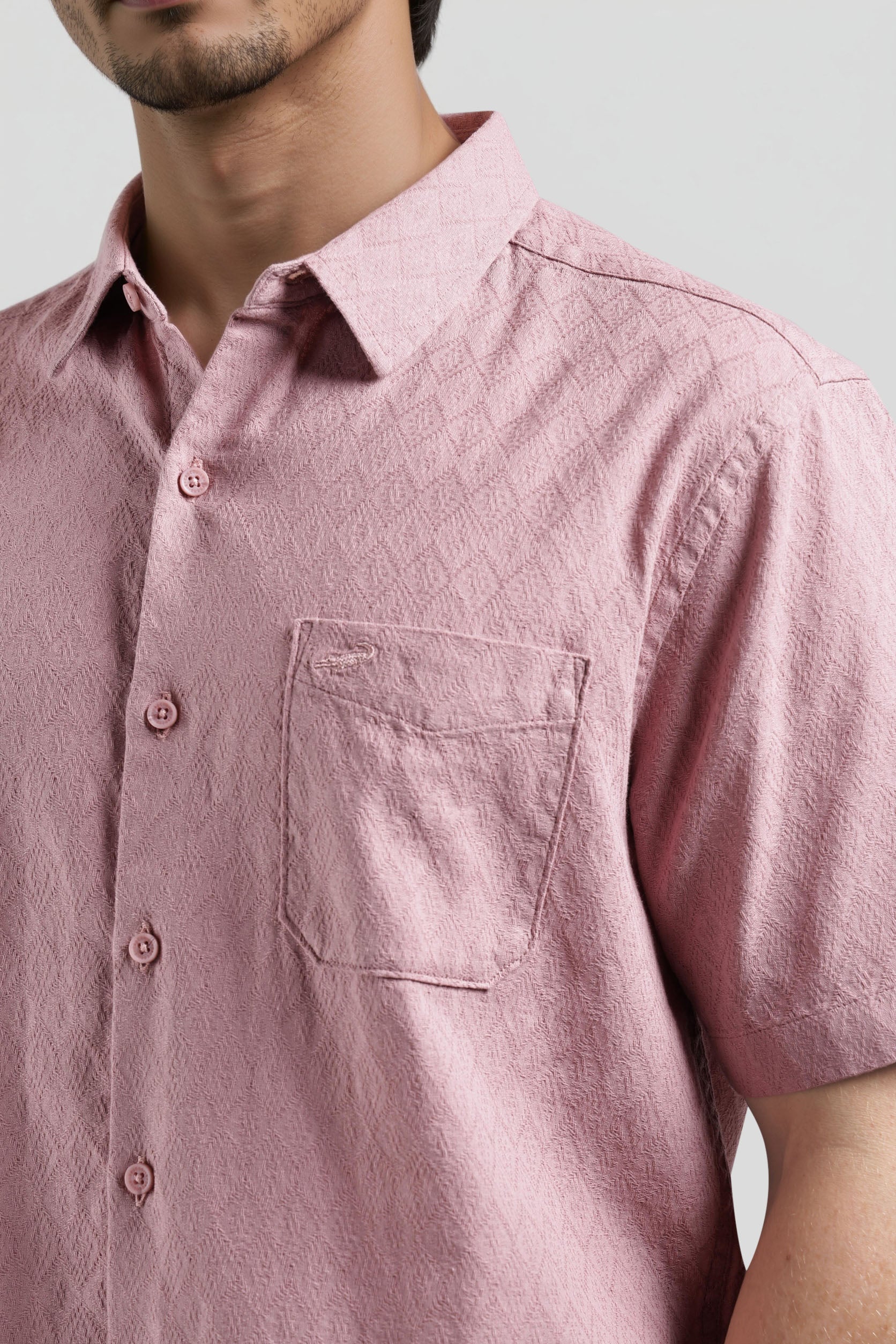 Close-up of a person wearing a pink short-sleeve shirt with a pocket on a light gray background