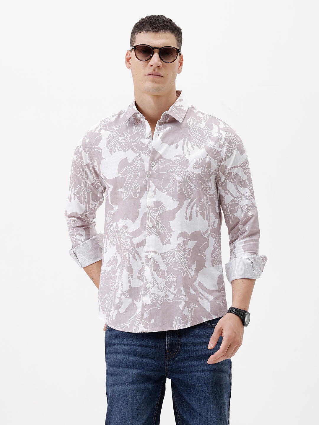 A man wearing a long-sleeve button-up shirt with a light gray and white abstract floral pattern, paired with dark blue jeans, standing against a plain white background.