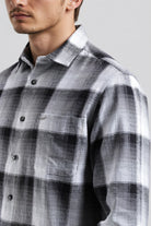 Man wearing a gray and white plaid shirt against a plain background