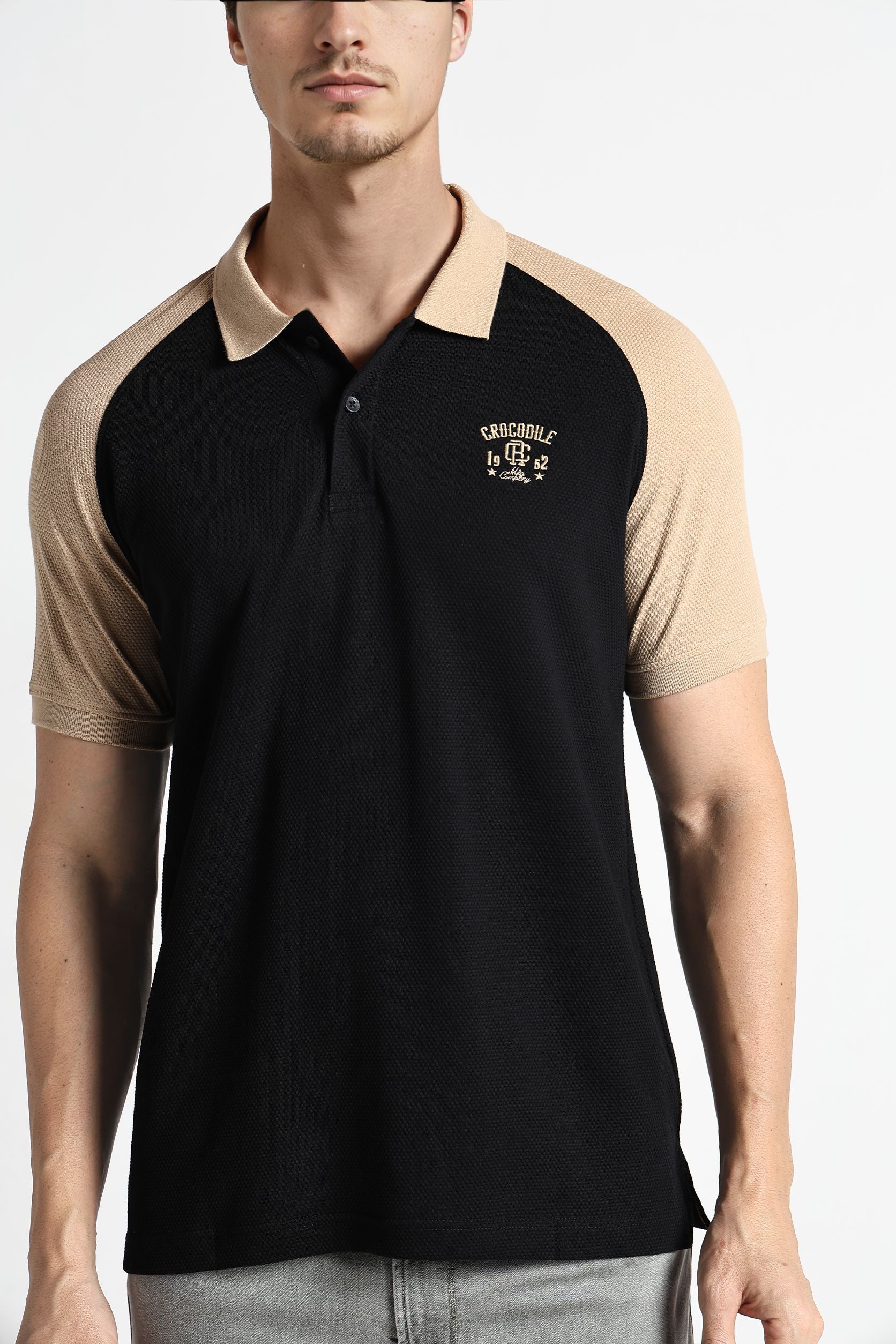 Man wearing a black and beige polo shirt with a logo on a white background