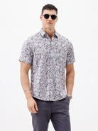 A man wearing a short-sleeve button-up shirt with a gray and white abstract pattern, paired with dark gray trousers, standing against a plain white studio background.