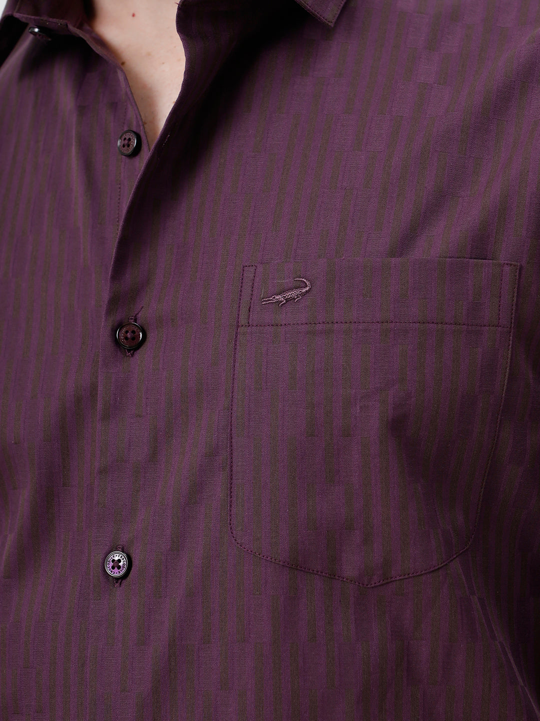 A man wearing a dark purple long-sleeve button-down shirt with subtle vertical stripes and dark navy trousers, standing against a light gray background.