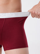 Maroon boxer briefs with white waistband being pulled by a hand on a light gray background