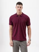 A man wearing a short-sleeve polo shirt in deep burgundy with a subtle textured geometric pattern, styled with gray trousers, sunglasses, and a watch against a plain white background.