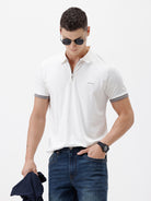 A man wearing a white short-sleeve polo shirt with gray ribbed trim on the collar and sleeve cuffs, paired with dark blue jeans, photographed against a plain white studio background.