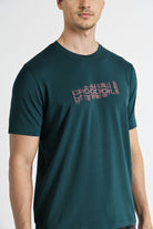 Man wearing a dark green t-shirt with a logo on a white background