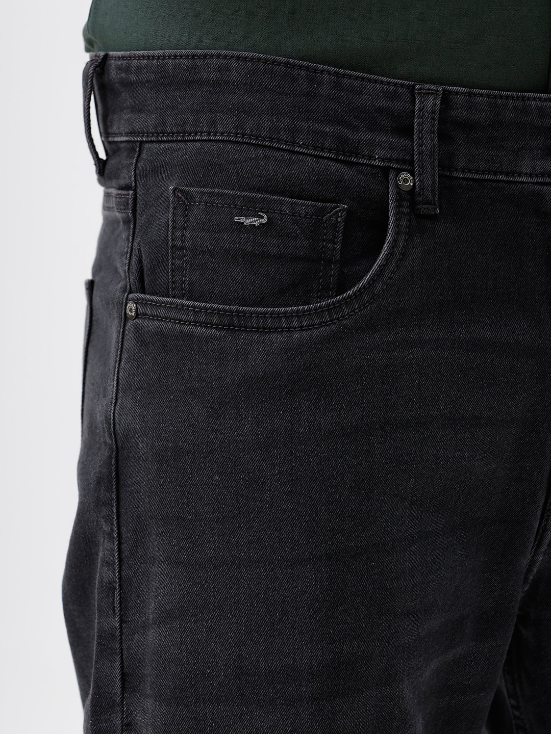 A person wearing dark washed denim jeans, a dark green shirt, and white sneakers, shown from the chest down against a plain light gray studio background.