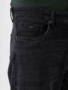 A person wearing dark washed denim jeans, a dark green shirt, and white sneakers, shown from the chest down against a plain light gray studio background.