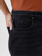 A person wearing black slim-fit jeans, paired with a rust-orange t-shirt and brown sneakers, shown from the waist down against a plain white studio background.