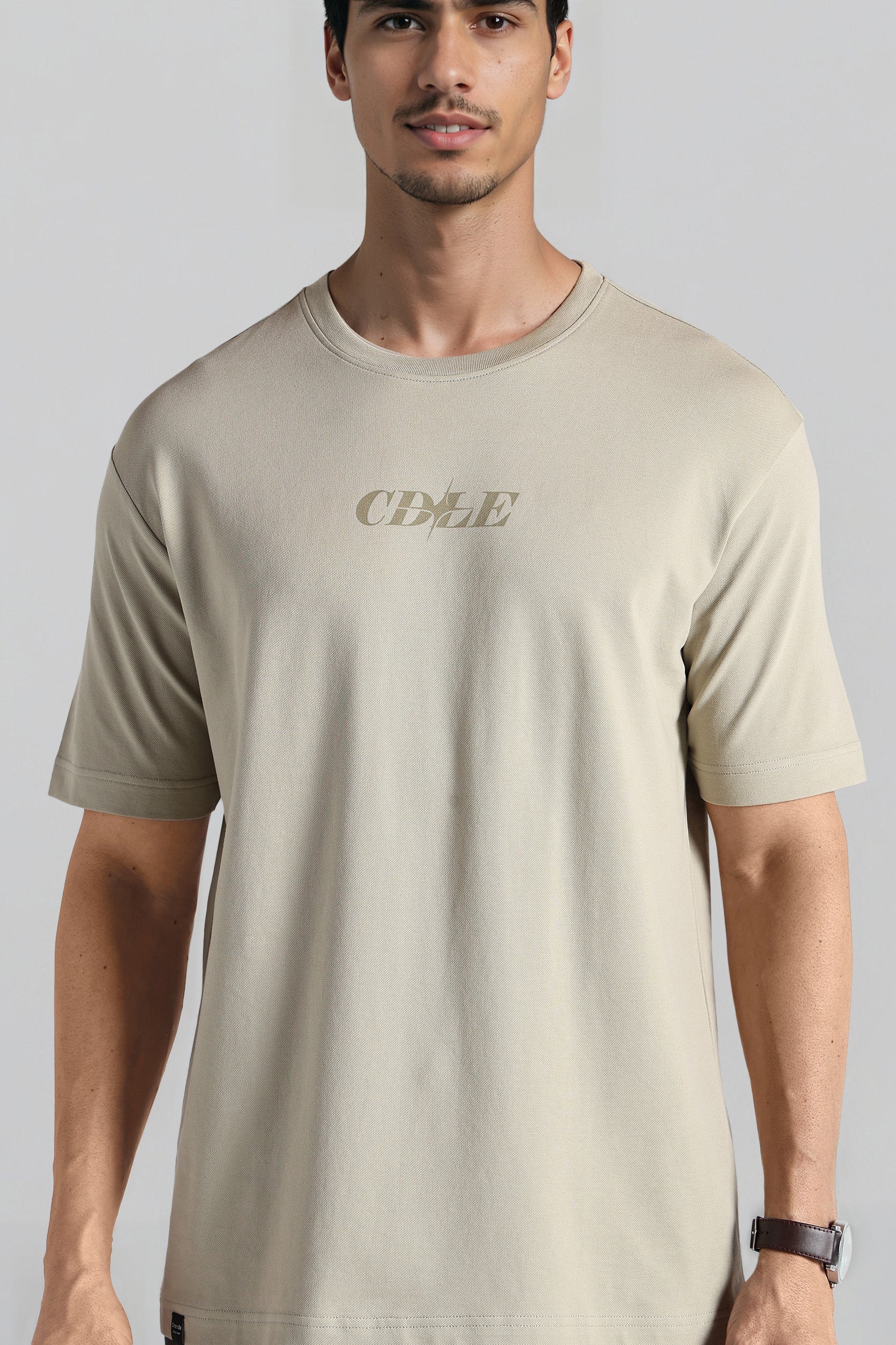 Man wearing a beige t-shirt with 'CDLE' logo on a gray background