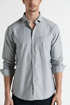 Man wearing a light gray button-up shirt with rolled-up sleeves on a white background