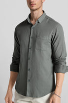 Man wearing a gray button-up shirt with rolled-up sleeves on a plain background