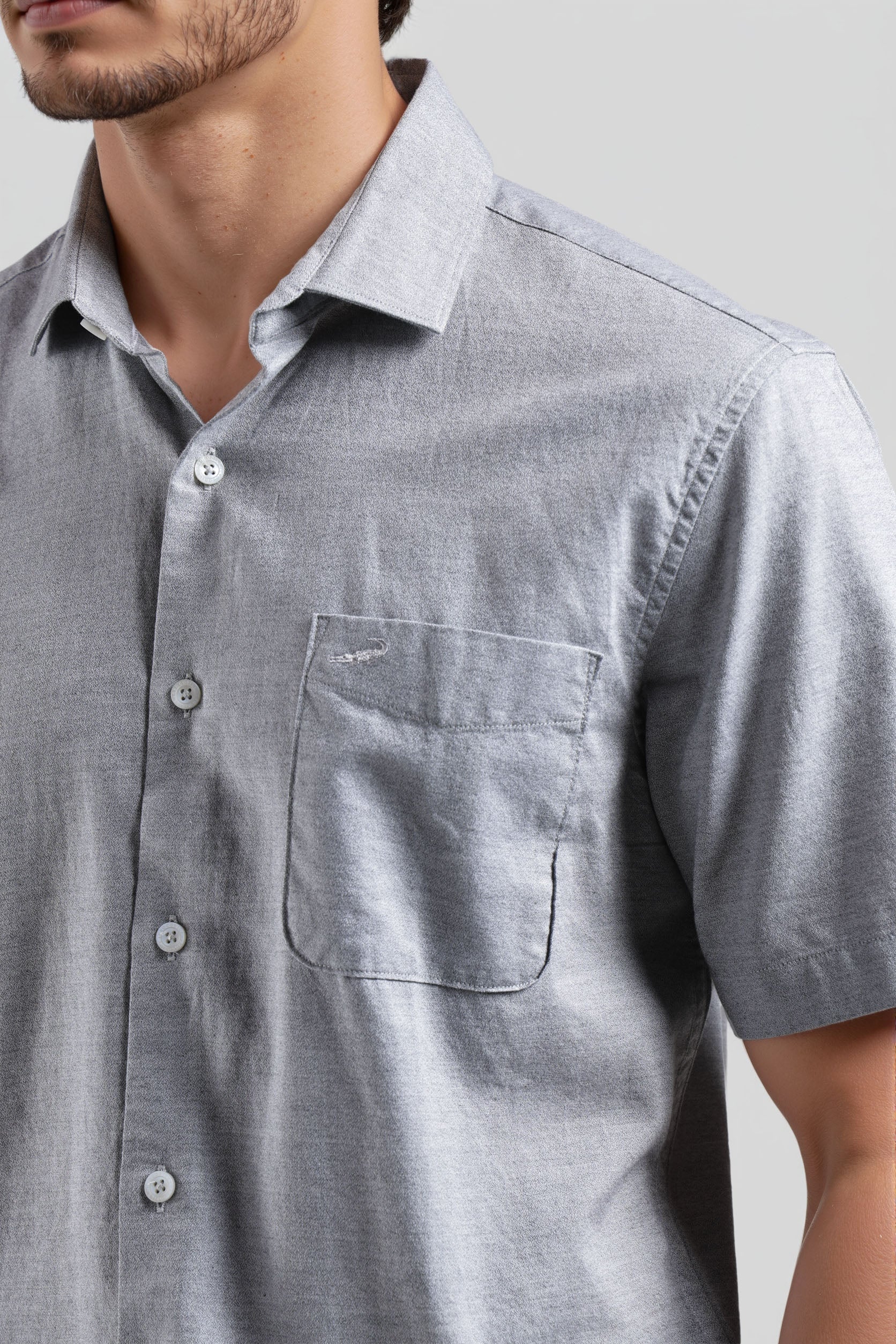 Close-up of a person wearing a gray short-sleeve shirt with a collar and pocket.