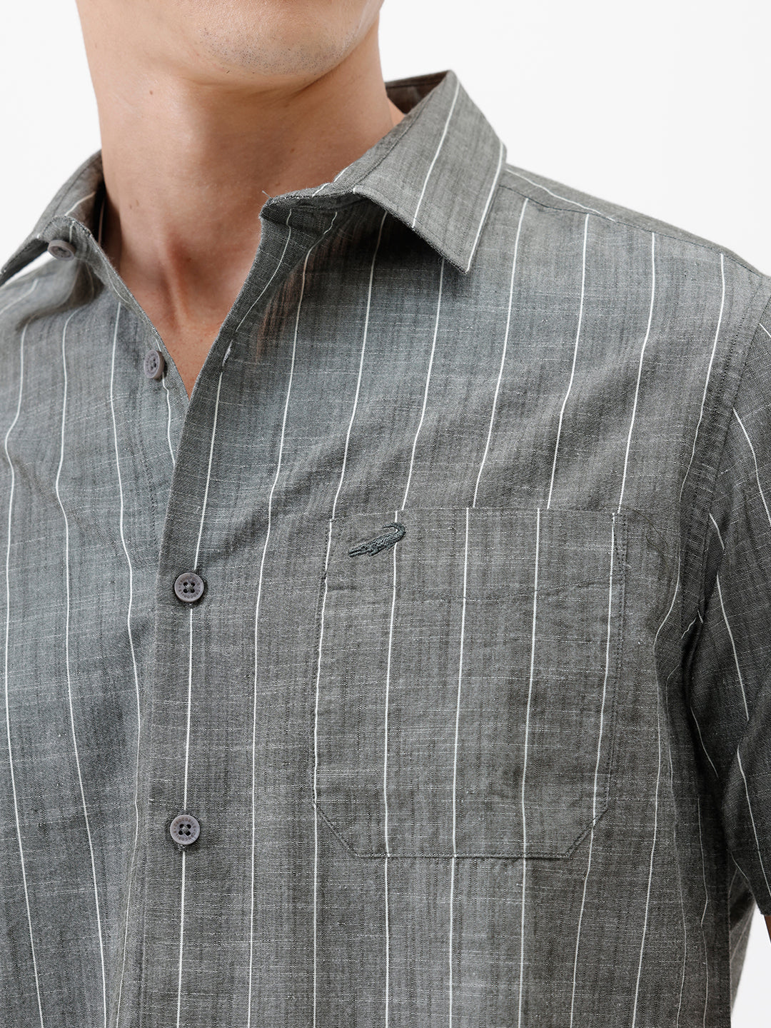 A man wearing a short-sleeve button-up shirt with a gray and white vertical stripe pattern, paired with black pants, standing against a plain white studio background.