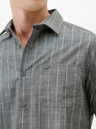 A man wearing a short-sleeve button-up shirt with a gray and white vertical stripe pattern, paired with black pants, standing against a plain white studio background.
