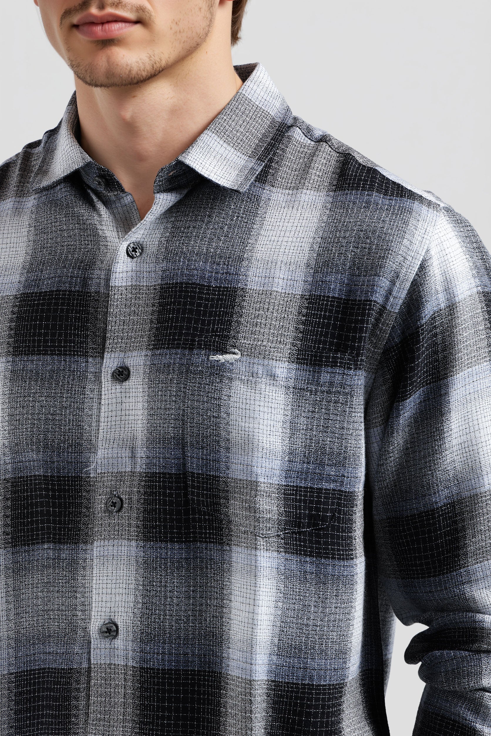 Man wearing a plaid shirt with a visible brand logo on a light gray background