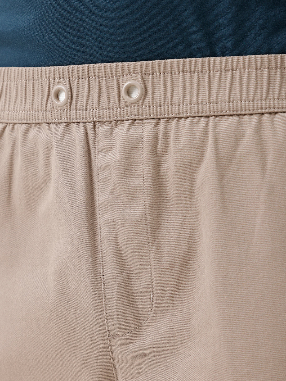 A person wearing beige drawstring shorts, a navy blue t-shirt, and white sneakers, shown from the waist down against a plain white studio background.