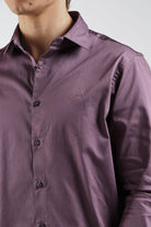 Close-up of a person wearing a purple shirt with a brand logo on a white background