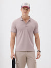 A man modeling a short-sleeve polo shirt in a dusty mauve-pink color, paired with khaki cargo pants and a baseball cap, against a plain light gray background.