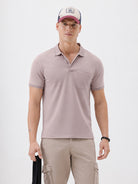 A man modeling a short-sleeve polo shirt in a dusty mauve-pink color, paired with khaki cargo pants and a baseball cap, against a plain light gray background.