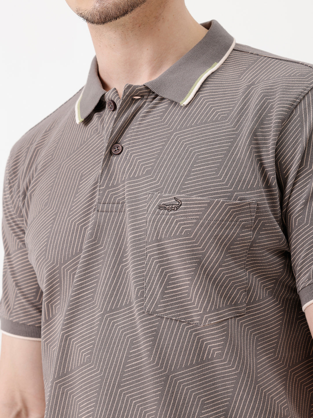 A man wearing a short-sleeve polo shirt with a gray and white geometric pattern, paired with beige trousers, standing against a plain white studio background.