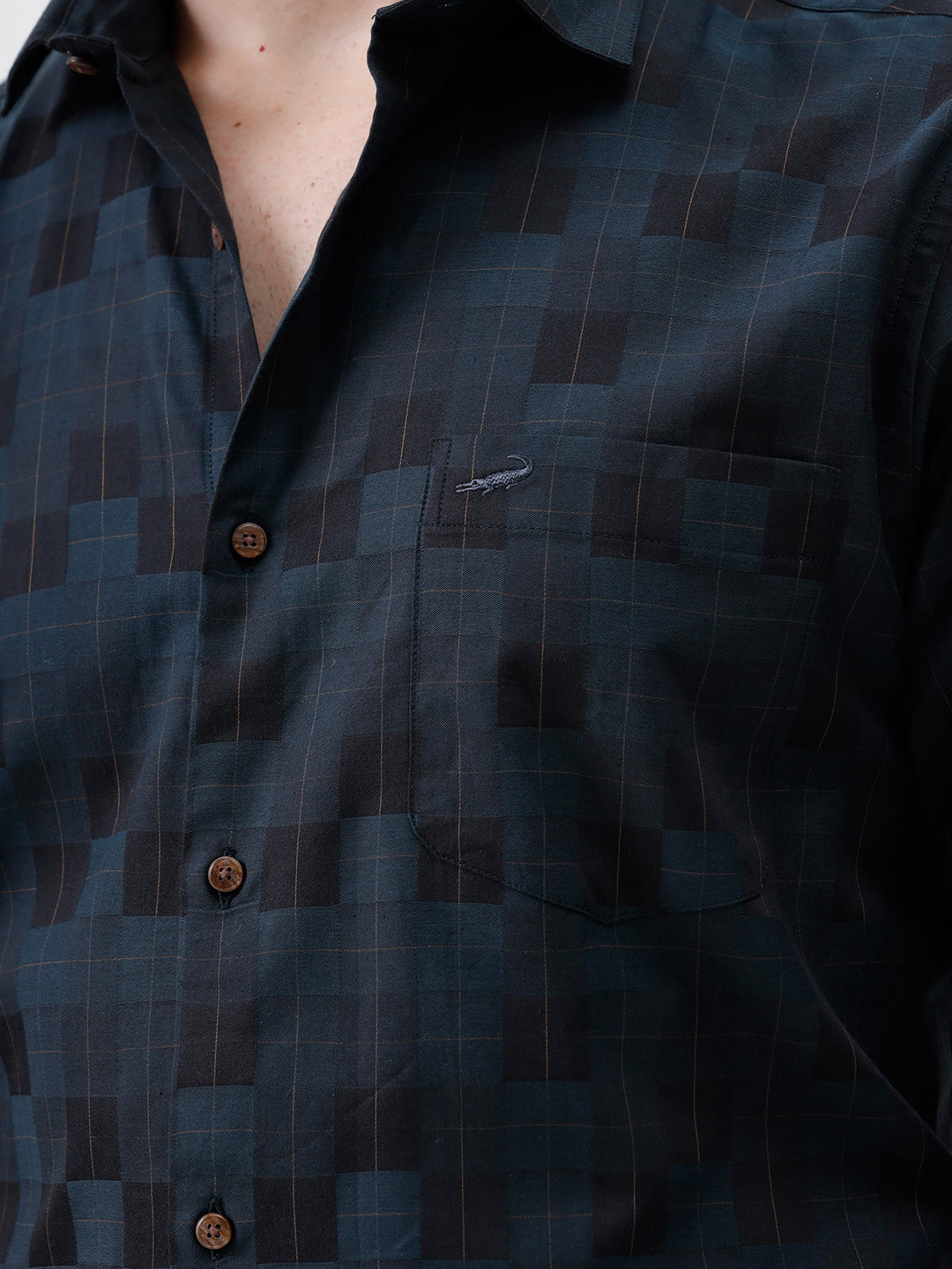 A man wearing a dark navy blue patterned long-sleeve button-up shirt and black trousers, standing against a plain white studio background.