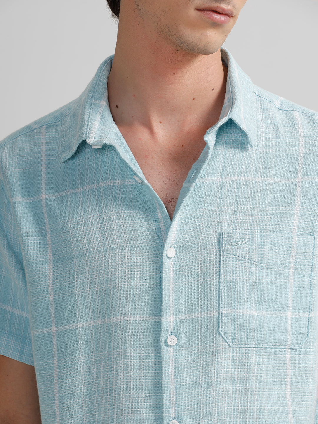 A man wearing a blue short-sleeved checkered shirt with a collar and a pocket on the chest.