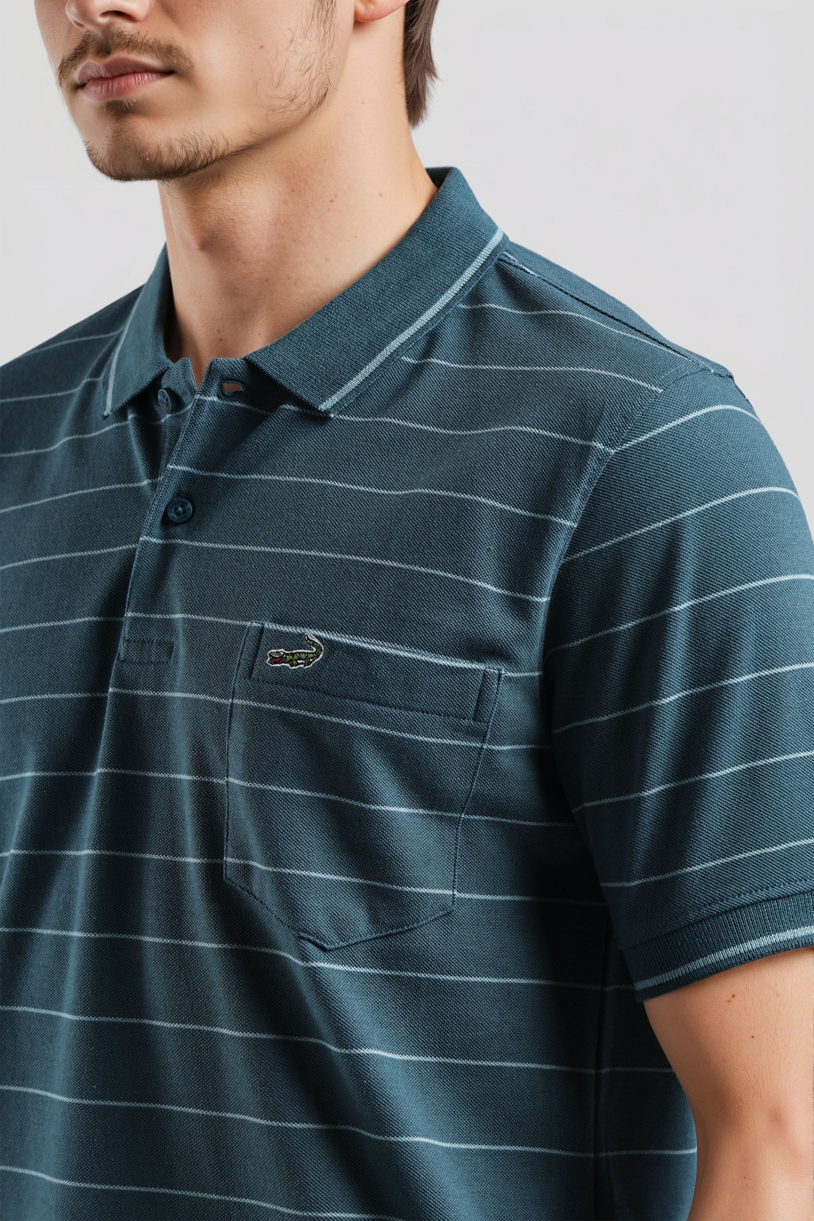 Man wearing a green striped polo shirt with a brand logo on a light gray background