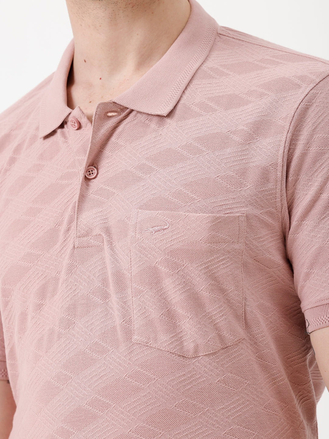 A man wearing a dusty pink short-sleeve polo shirt with a chest pocket, paired with light beige trousers, standing against a plain white studio background.