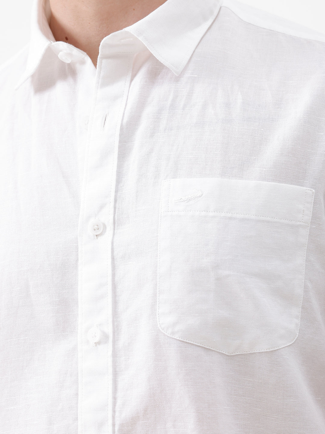 A man wearing a white short-sleeve button-up shirt with a chest pocket and beige trousers, standing against a plain white studio background.