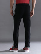 Person wearing black track pants with white stripes on a gray background