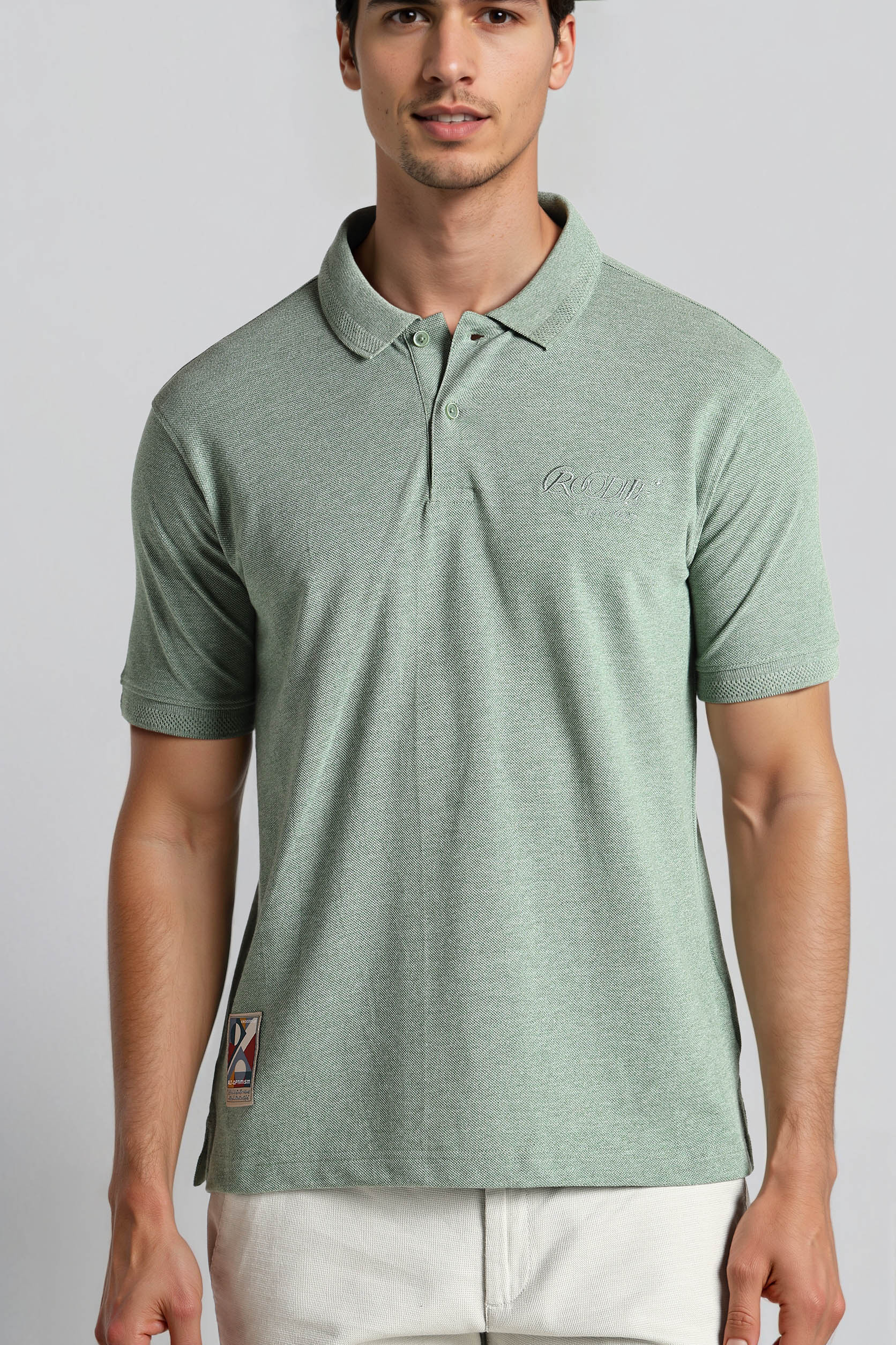 Man wearing a green polo shirt with a logo on a plain background