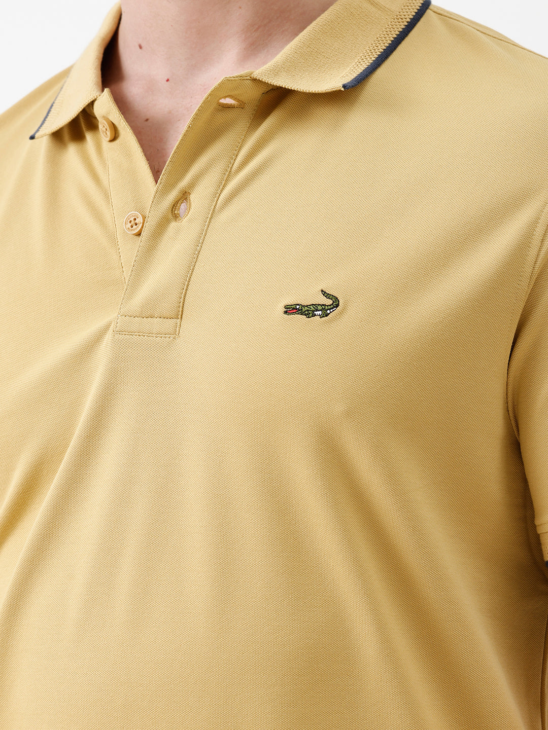 A man wearing a light yellow Lacoste polo shirt with dark piping on the collar and sleeve cuffs, paired with beige trousers, against a plain white studio background.