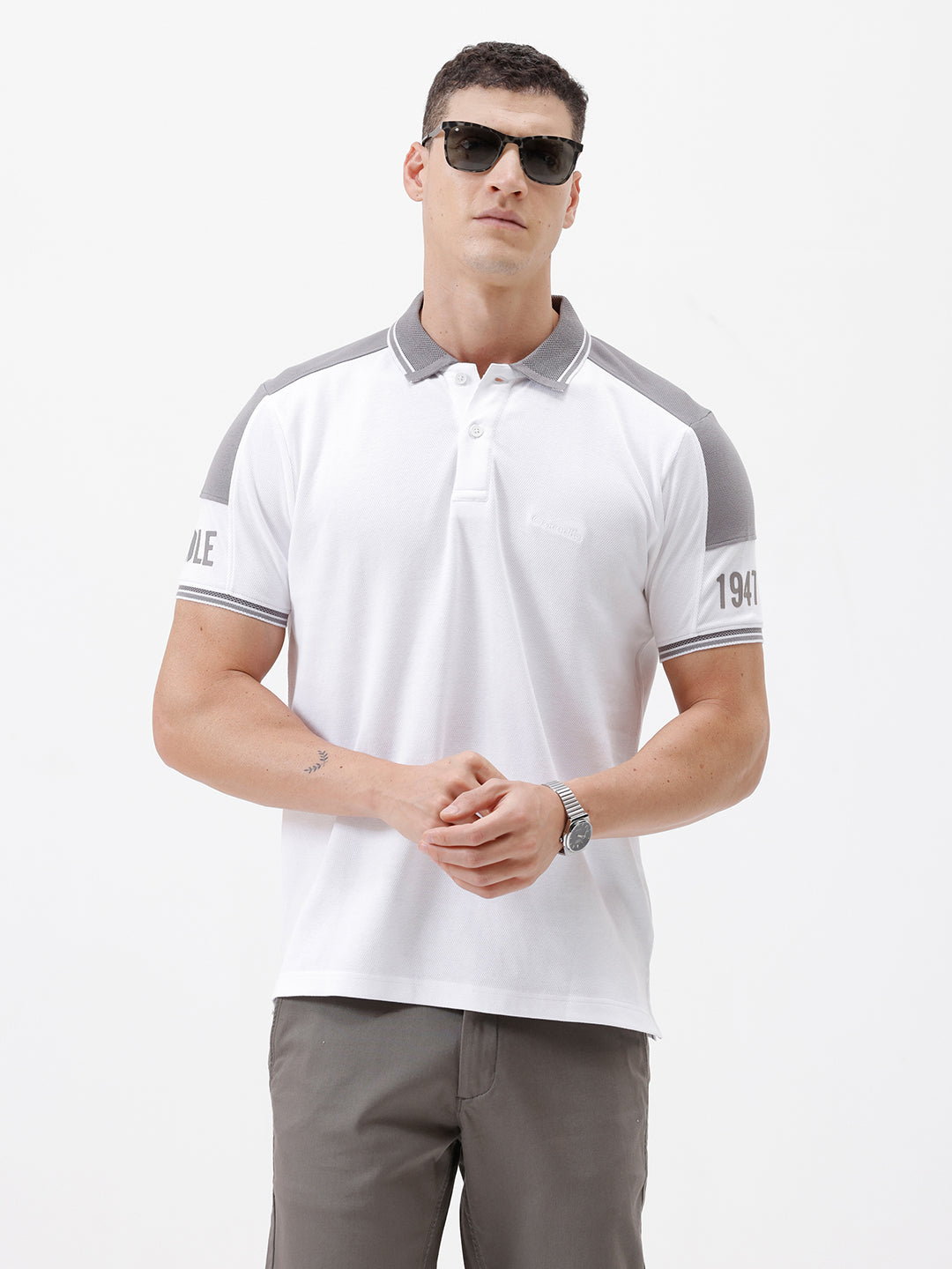 A man modeling a white short-sleeve polo shirt with gray shoulder panels and gray striped trim on the sleeves, paired with gray trousers and black sunglasses, against a plain white background.