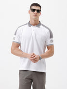 A man modeling a white short-sleeve polo shirt with gray shoulder panels and gray striped trim on the sleeves, paired with gray trousers and black sunglasses, against a plain white background.