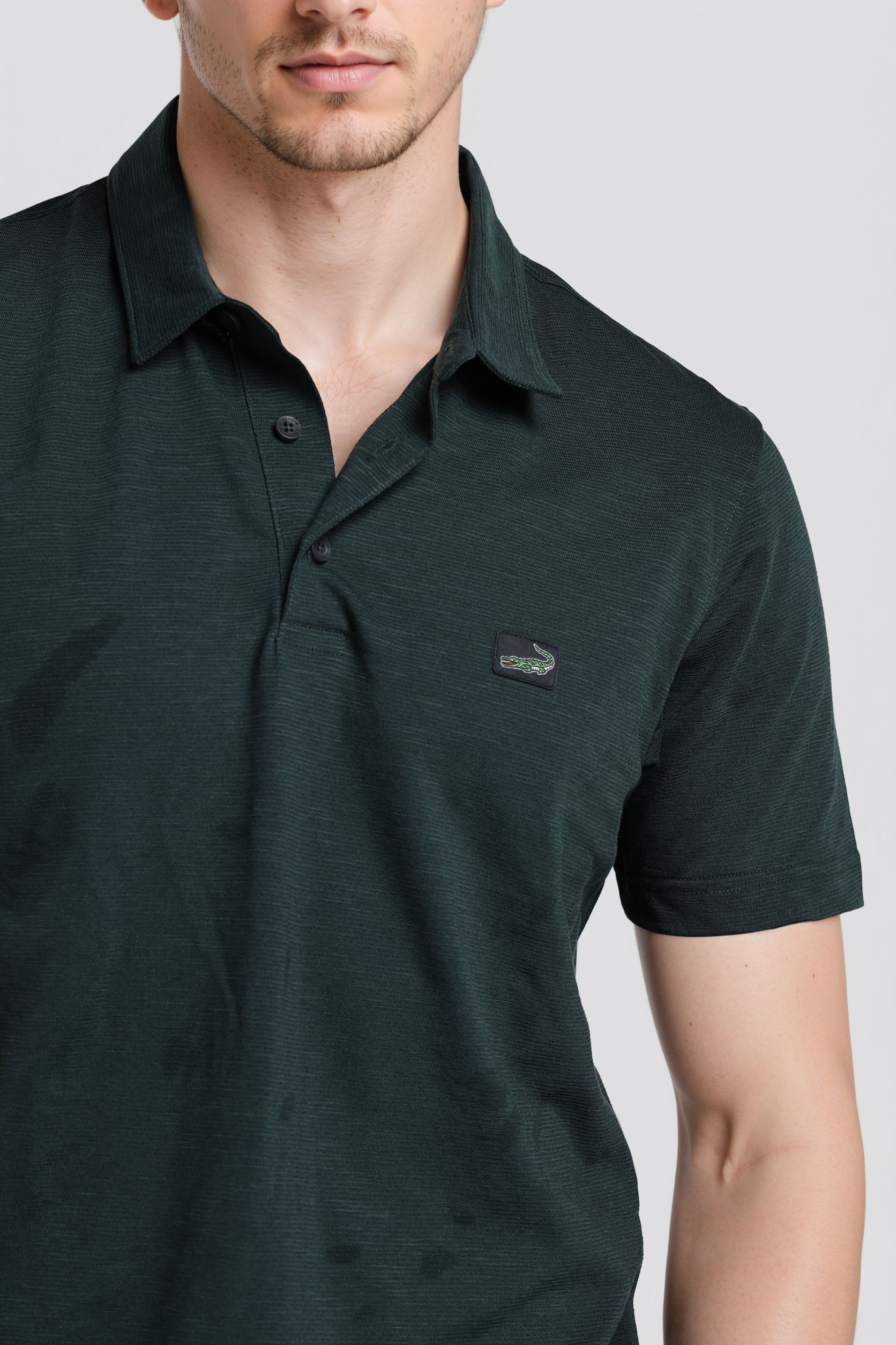 Man wearing a dark green polo shirt with a small logo on a light gray background