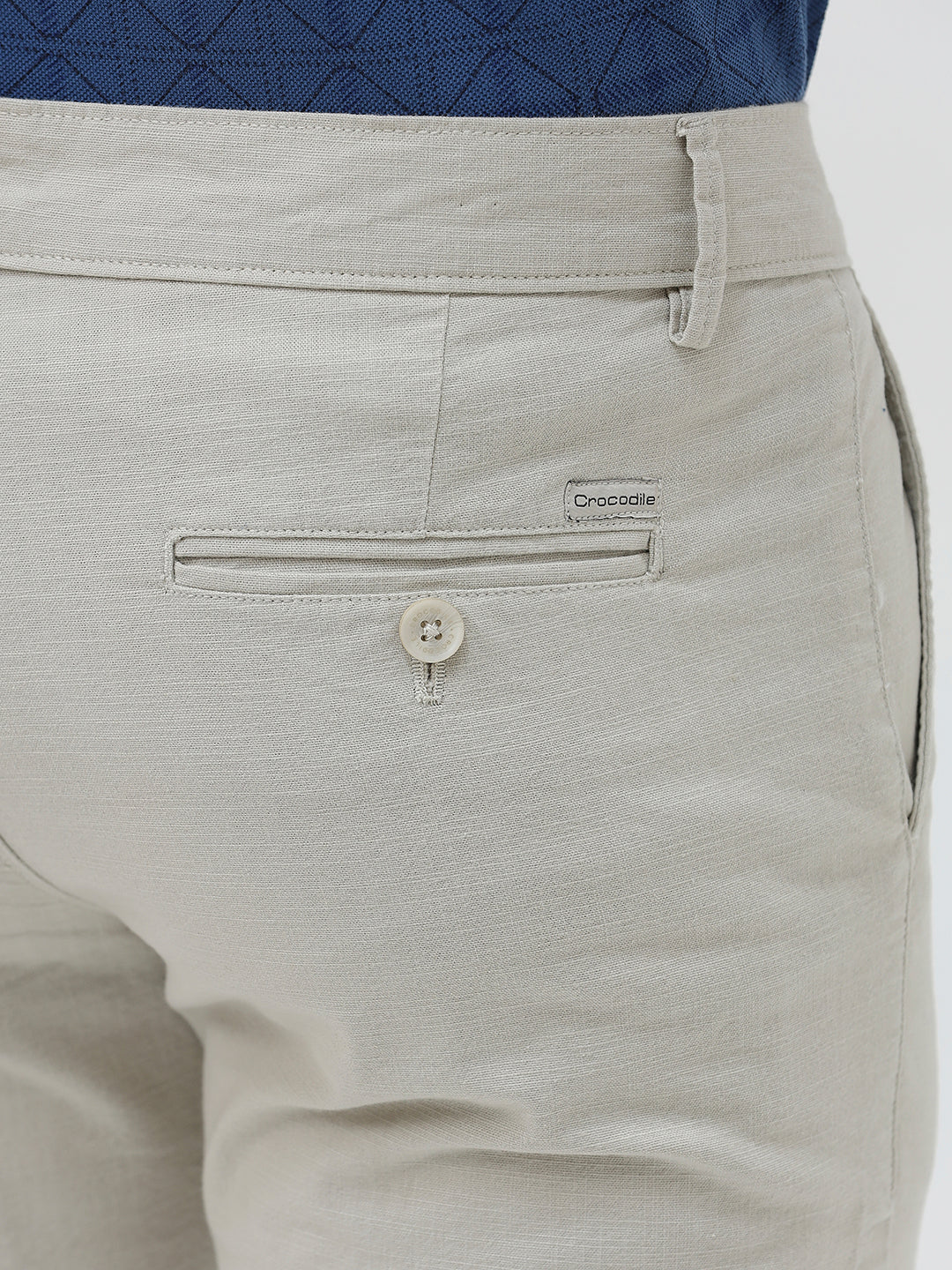 A person wearing light beige slim-fit chino pants, a navy blue t-shirt, and white sneakers, standing against a plain white studio background.