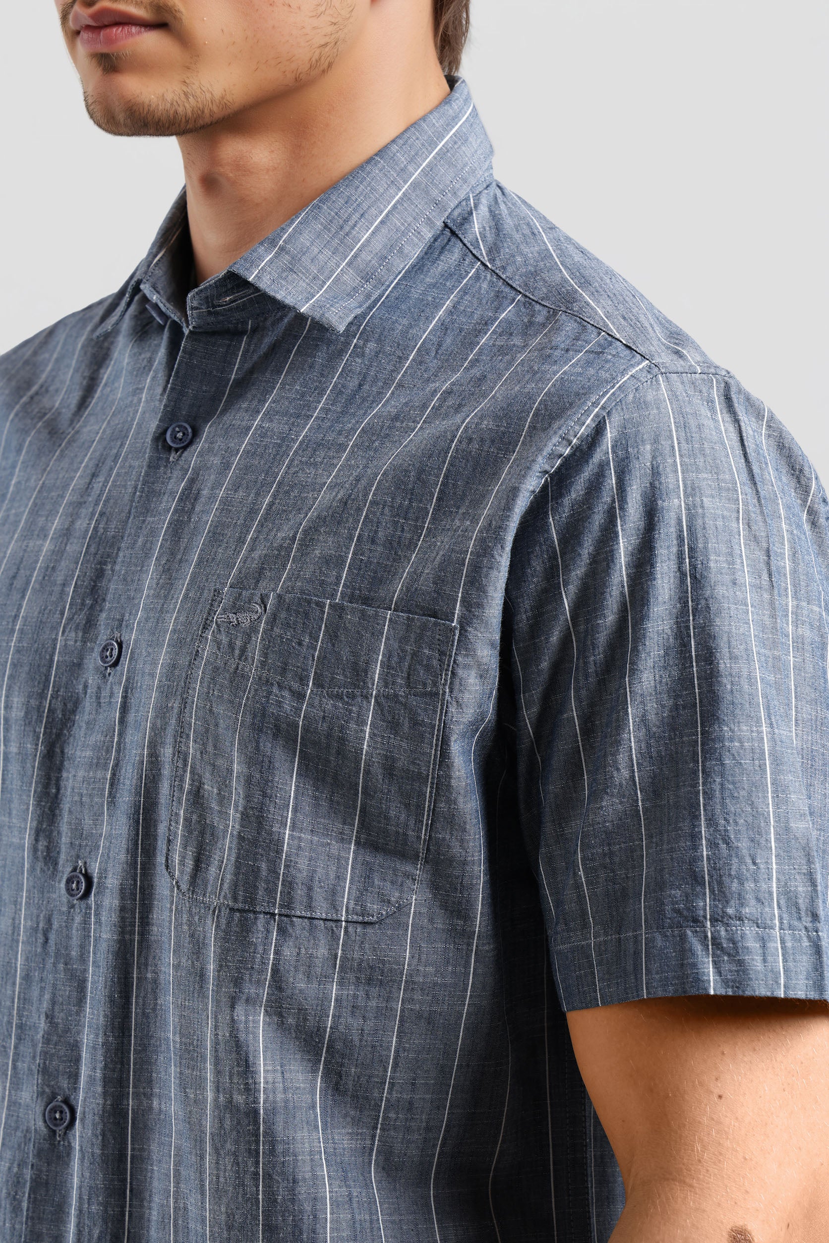 Close-up of a person wearing a blue striped shirt with a pocket on a gray background