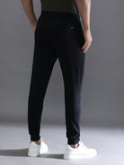 Person wearing black jogger pants and white sneakers on a gray background