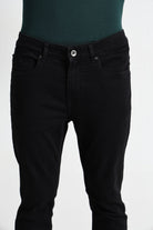 Black jeans worn over a green top on a white background